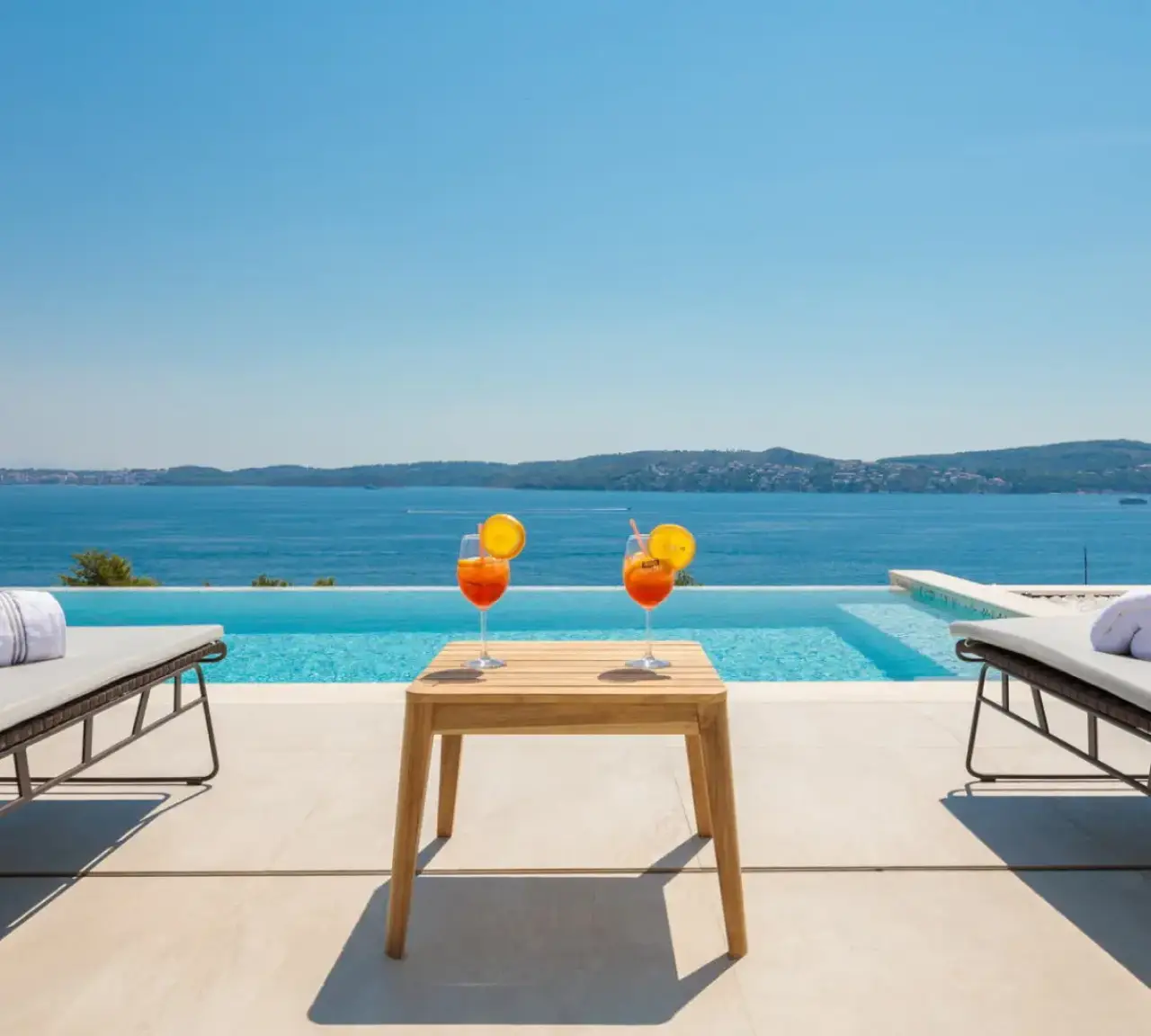 A villa terrace with a pool, sun loungers and an open sea view